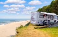 Zwei Wohnmobile stehen auf einer Wiese am Strand mit ausgeräumten Campingequipment.