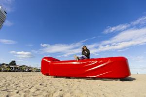 Eine Frau sitzt auf der Riesenwärmflasche Wärmy am Strand von Travemünde