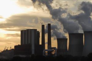 Silhouette eines Kohlekraftwerks mit aufsteigendem Rauch vor einem Sonnenuntergang