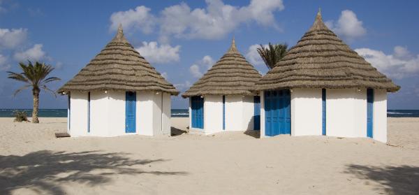 Weiße Hütten an einem Strand auf Djerba mit dem Meer im Hintergrund.