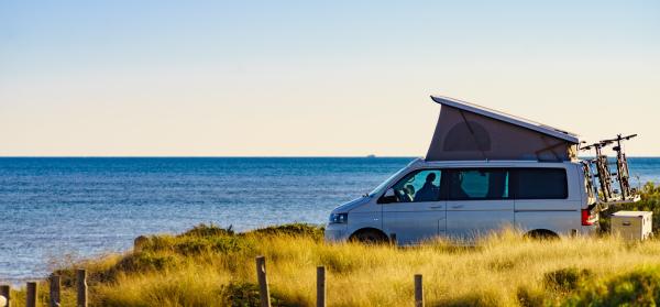 Campervan mit aufgestelltem Dachzelt an der Küste und mit Meer im Hintergrund.