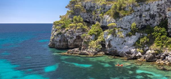 Cala Macarelleta auf Menorca mit Kajakfahrern im Hintergrund.