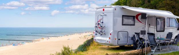Zwei Wohnmobile stehen auf einer Wiese am Strand mit ausgeräumten Campingequipment.