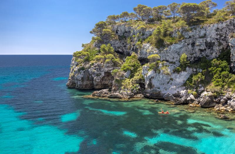 Cala Macarelleta auf Menorca mit Kajakfahrern im Hintergrund.