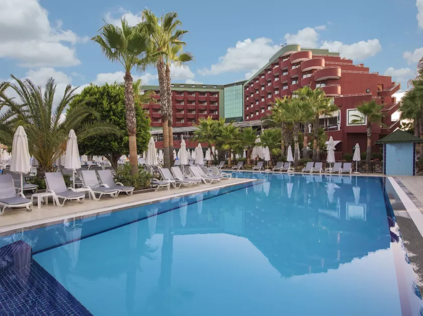 Luxuriöses Resort mit großer Poollandschaft, Palmen und modernen roten Gebäuden unter blauem Himmel.